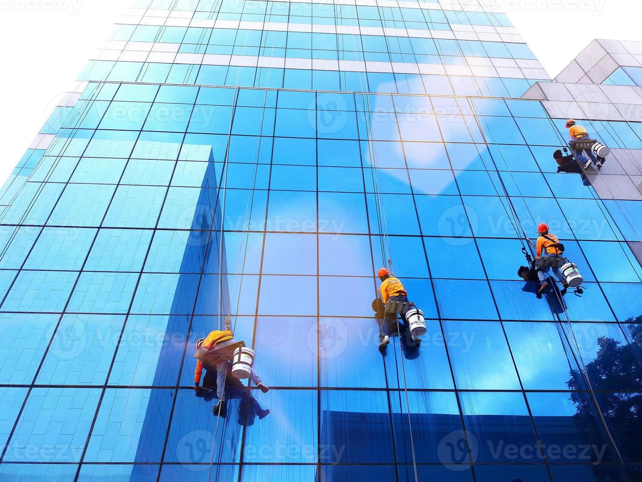 Bangkok, Thailand - October 16, 2017 Group of cleaner hanging, washing and cleaning windows on high rise building with orange sunlight flare - High building and Risk working. photo