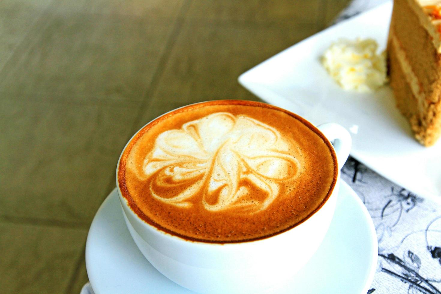 Cup of hot cappuccino coffee on the table with blurred cake and whipped cream background photo