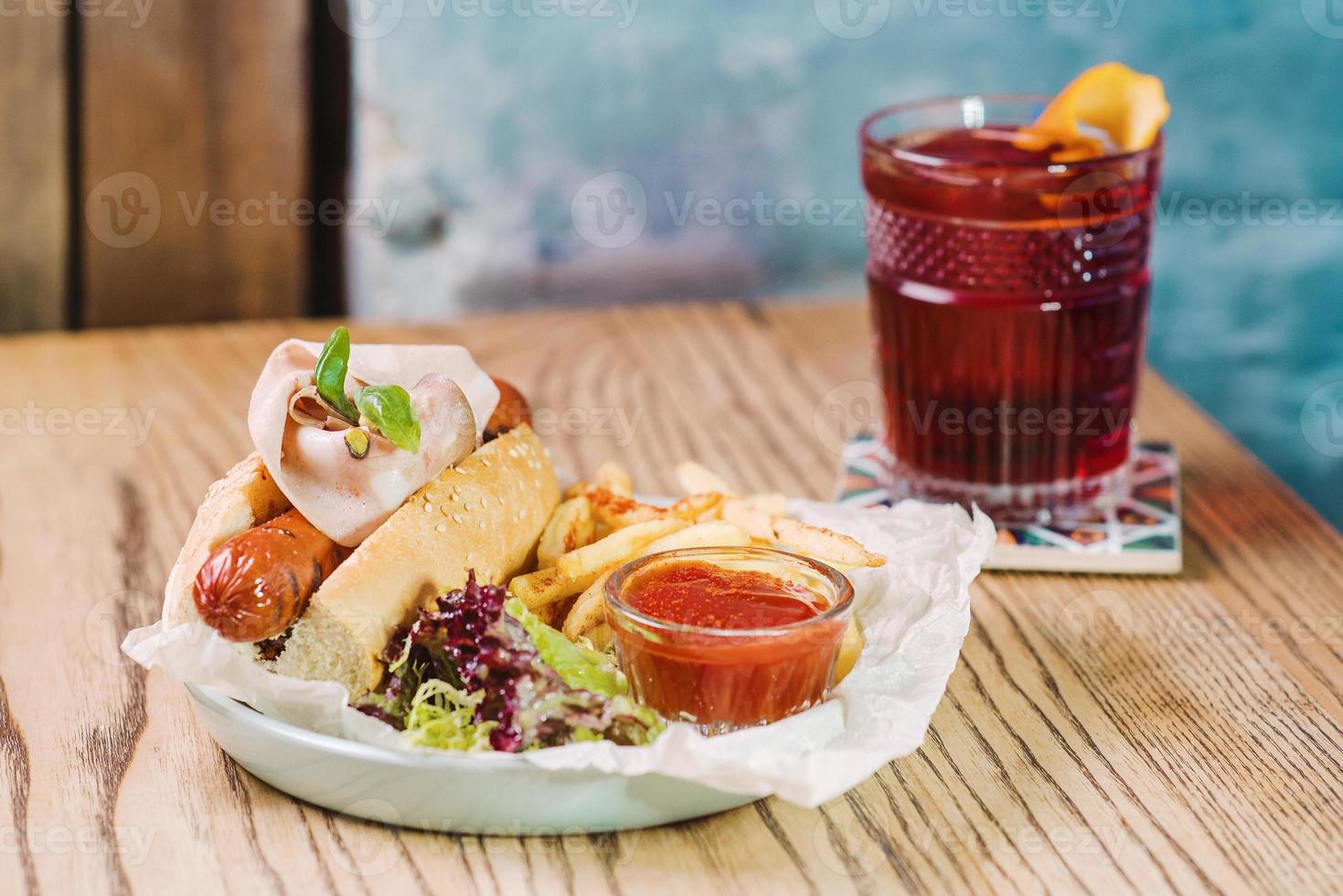 plato con hot dog con salchicha y jamón, salsa de tomate ketchup y cóctel frito a la antigua y sobre la mesa en el bar foto