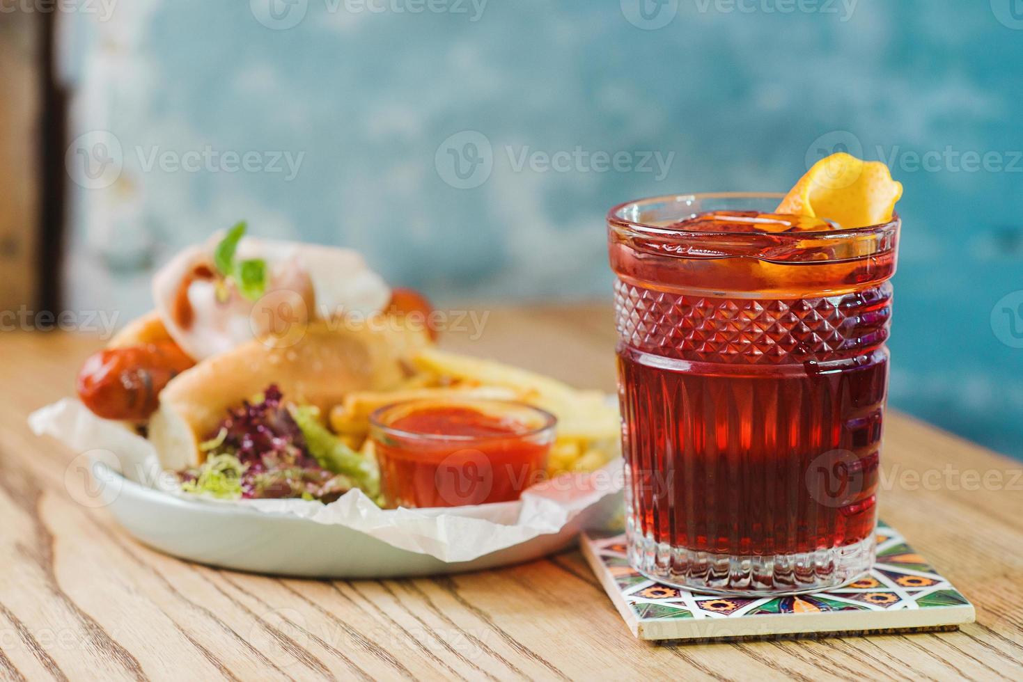 plate with hot dog with sausage and ham, tomato sauce ketchup and french friedold fashioned cocktail and  on the table in the bar photo