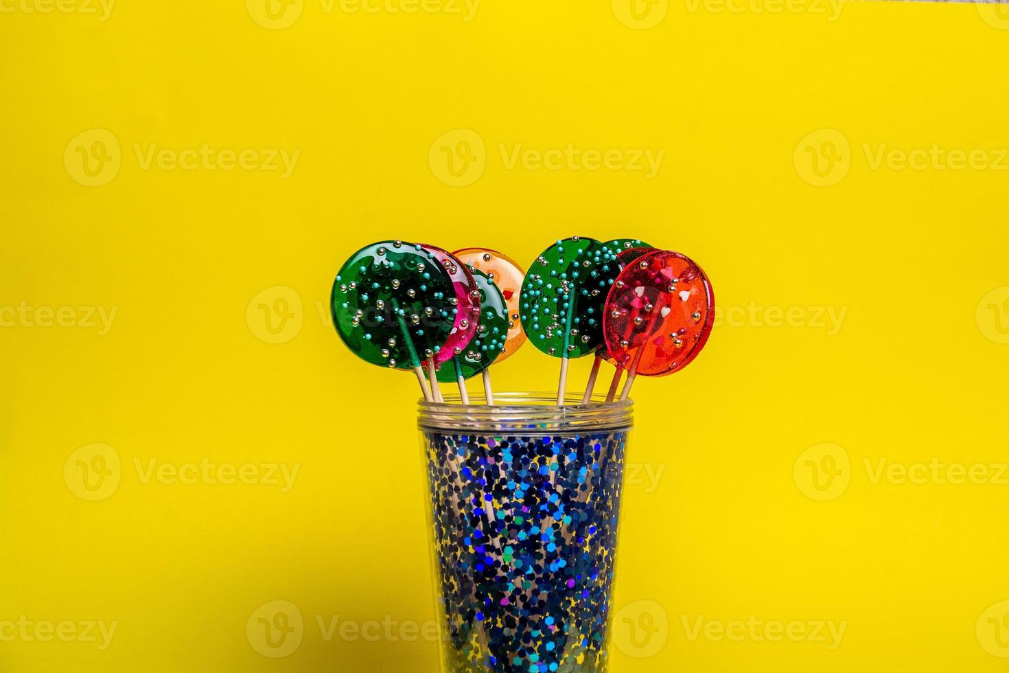 multi-colored lollipops in a blue glass on a yellow background. photo