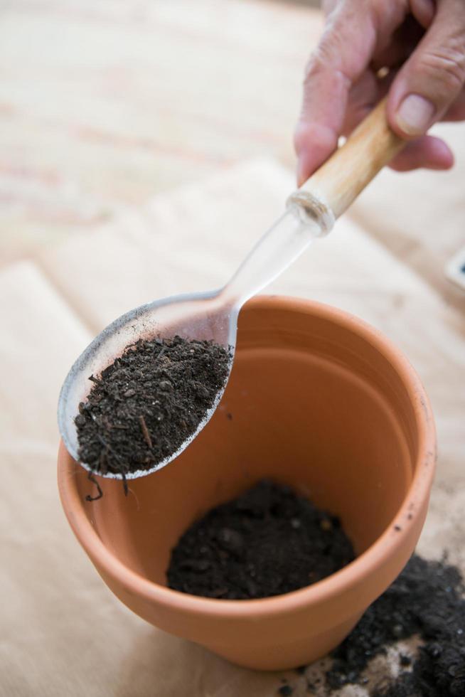 Human hand with a big spoon adding soil to a clay pot. Directly above. photo