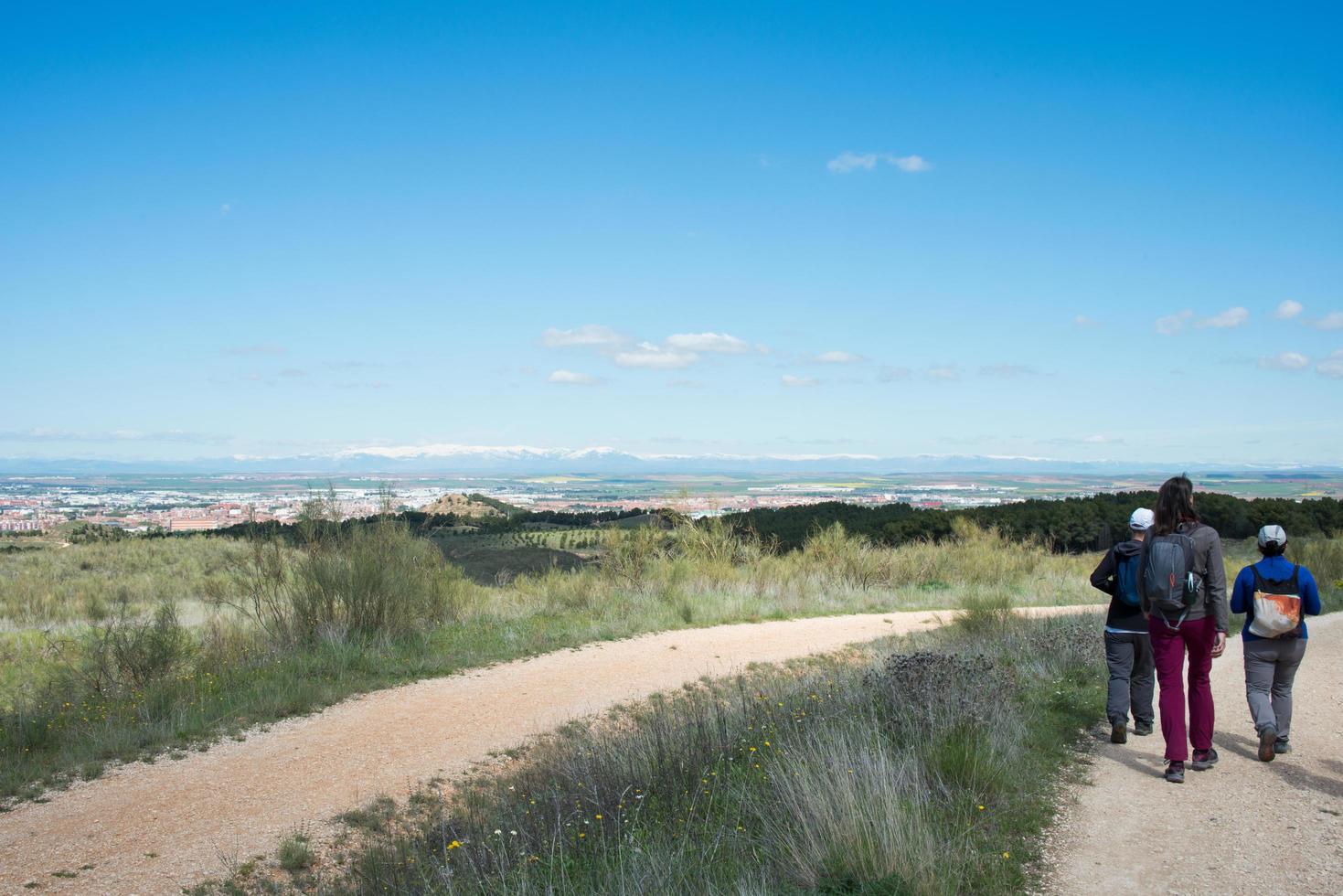 Group of three people with hiking clothes walking in Los Cerros Park. Seen from their back. Alcala de Henares, Madrid photo