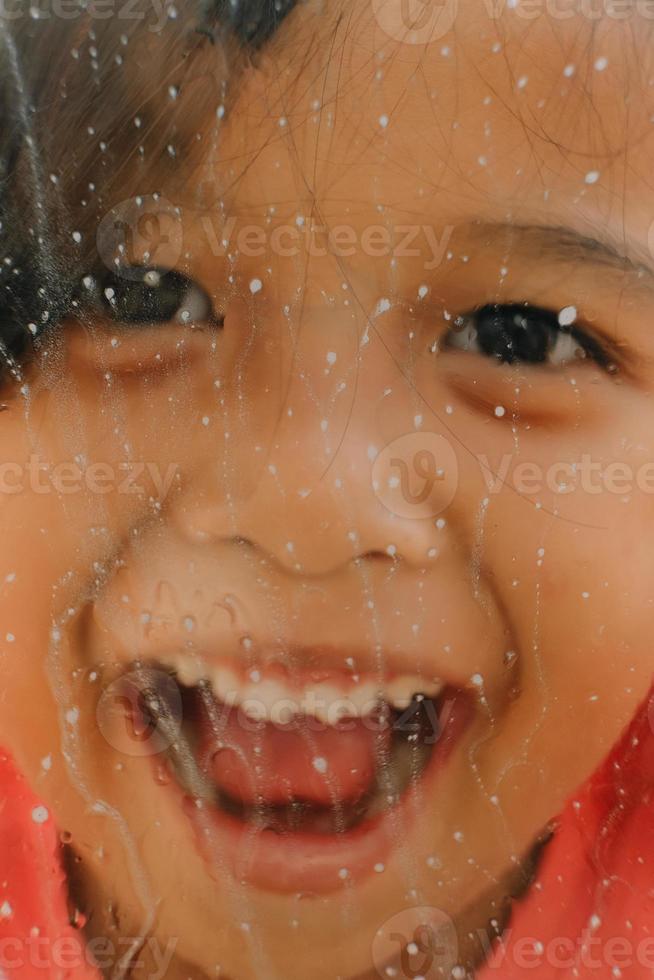 Portrait of a happy little girl behind the glass photo