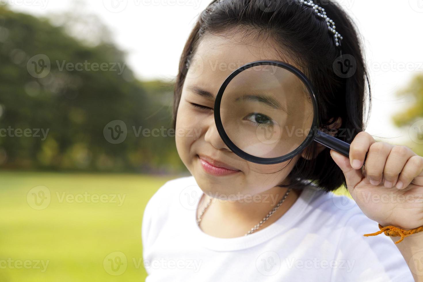 Asian little girl holding a magnifying glass in outdoor photo