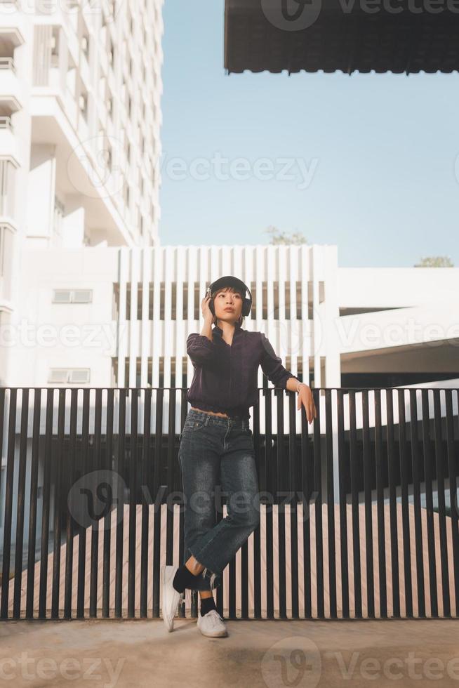 Happy young asian woman listening to music and having fun with headphones on the street photo