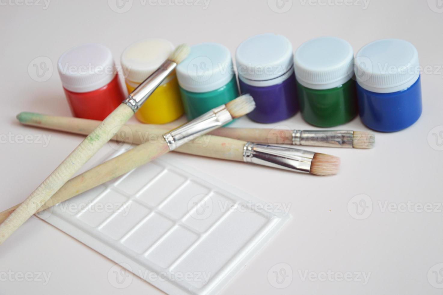 Multi-colored gouache paint in closed jars and a set of artistic brushes. Drawing materials, hobbies, tools, artist's palette. photo