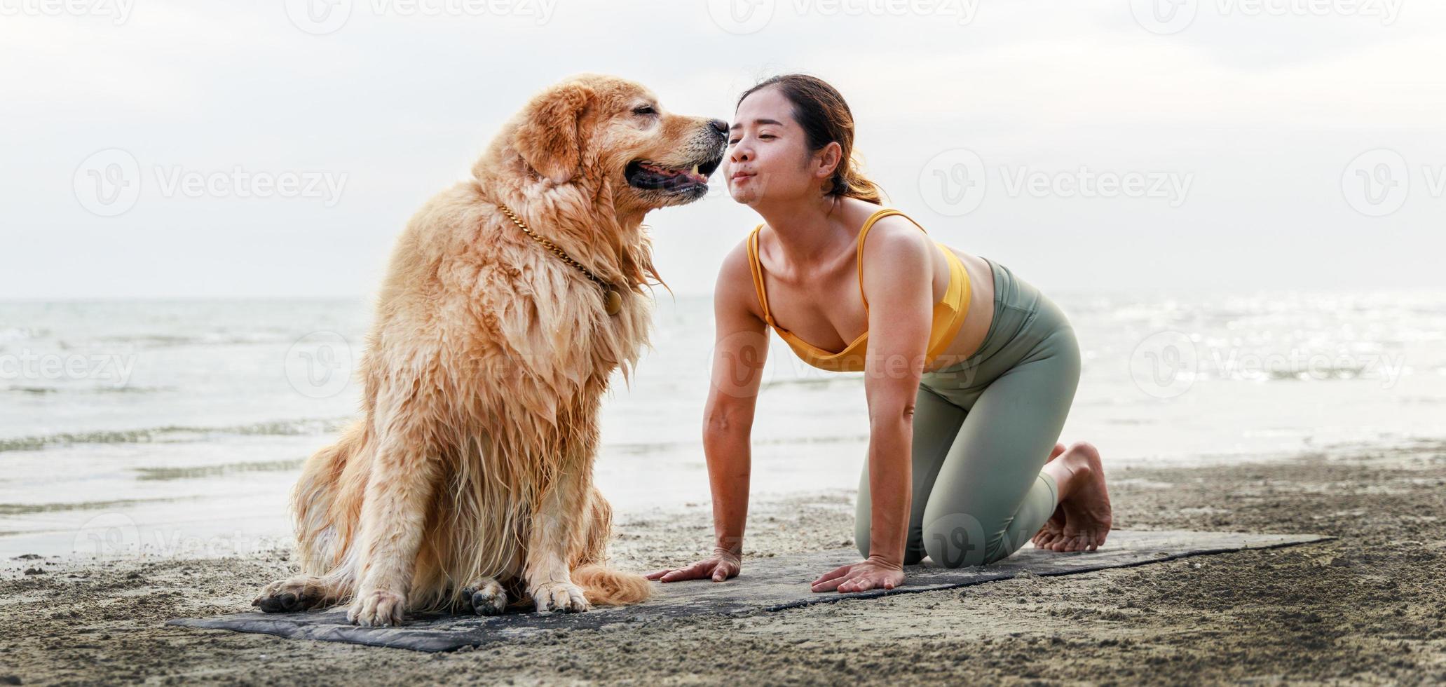 Asian young woman kisses her dog during doing yoga on a yoga mat on the beach. Relaxation with a pet. photo