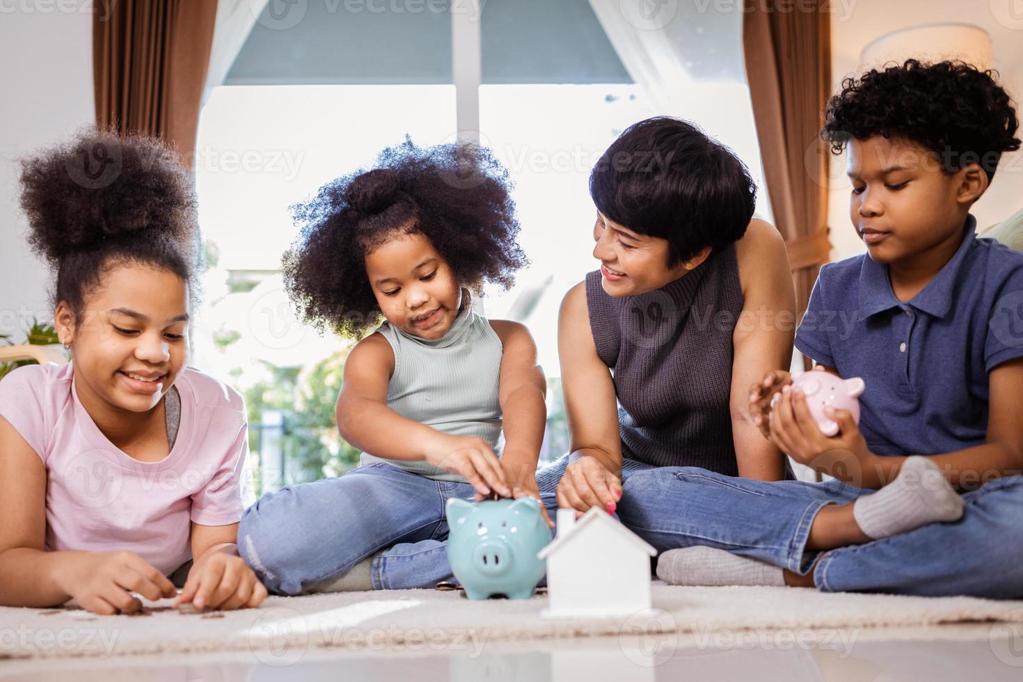 niños afroamericanos felices y madre poniendo una moneda en una alcancía juntos en casa foto