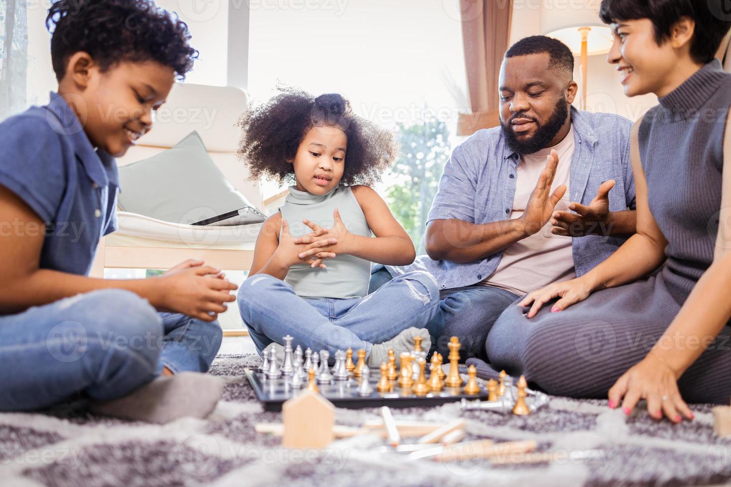 Two African American kids with mother and father playing a game of Chess and having fun together photo