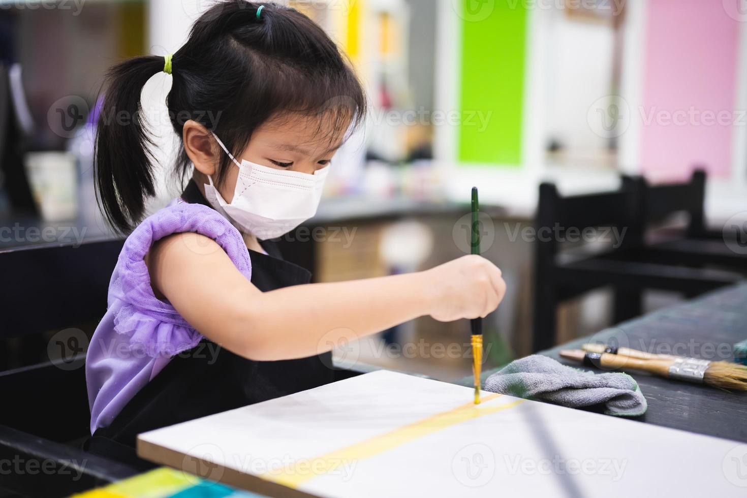 Kindergarten kid learning art water color. Children wearing white medical face mask to reduce spread of virus. photo