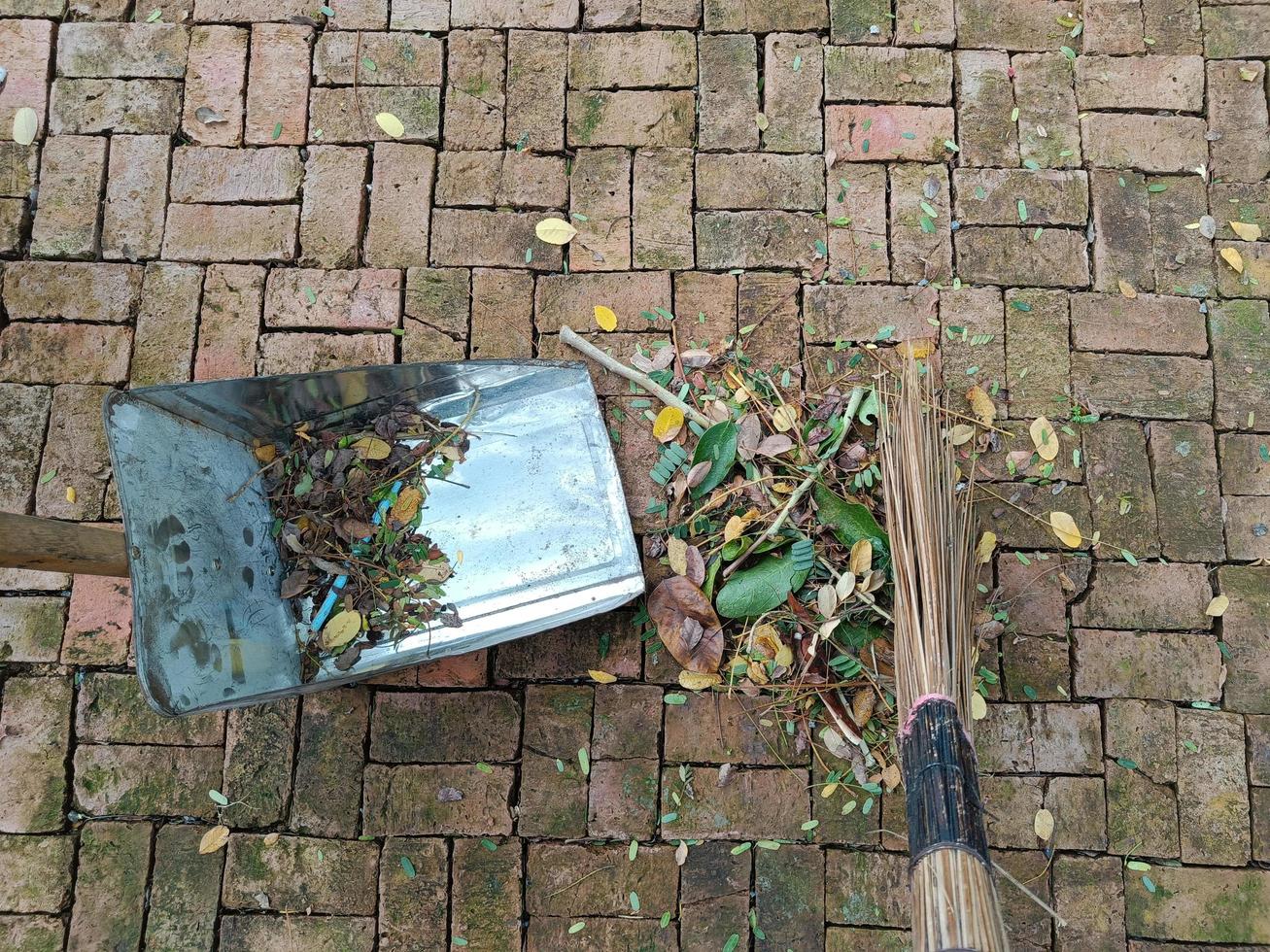 Sweeping dry leaves with broom, garden, Maintenance worker in park garden cleans the roads photo