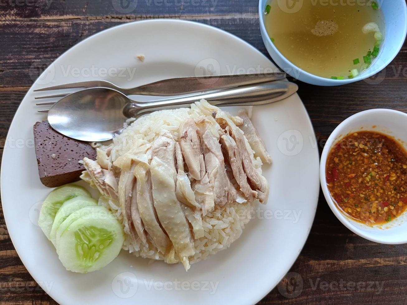 Hainanese chicken rice eat with chicken soup and sauce on a wooden background photo