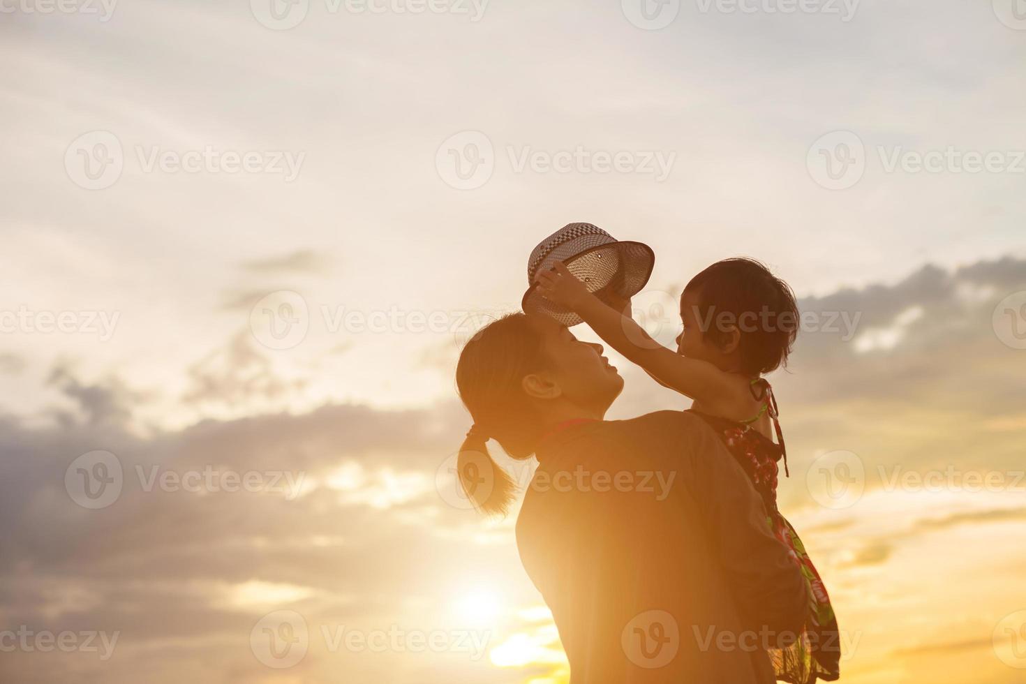 a silhouette of a happy young girl child the arms of his loving mother for a hug, in front of the sunset in the sky on a summer day. photo