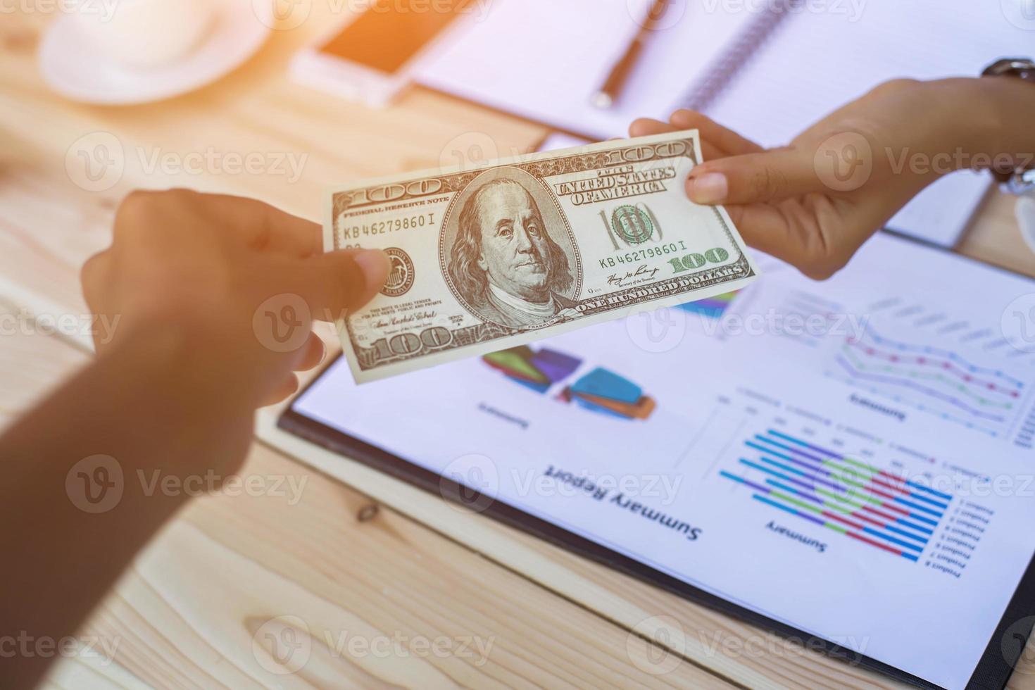 Business woman gripping The United States hundred-dollar bills in her hand and some put on the table full with business charts and notebook photo