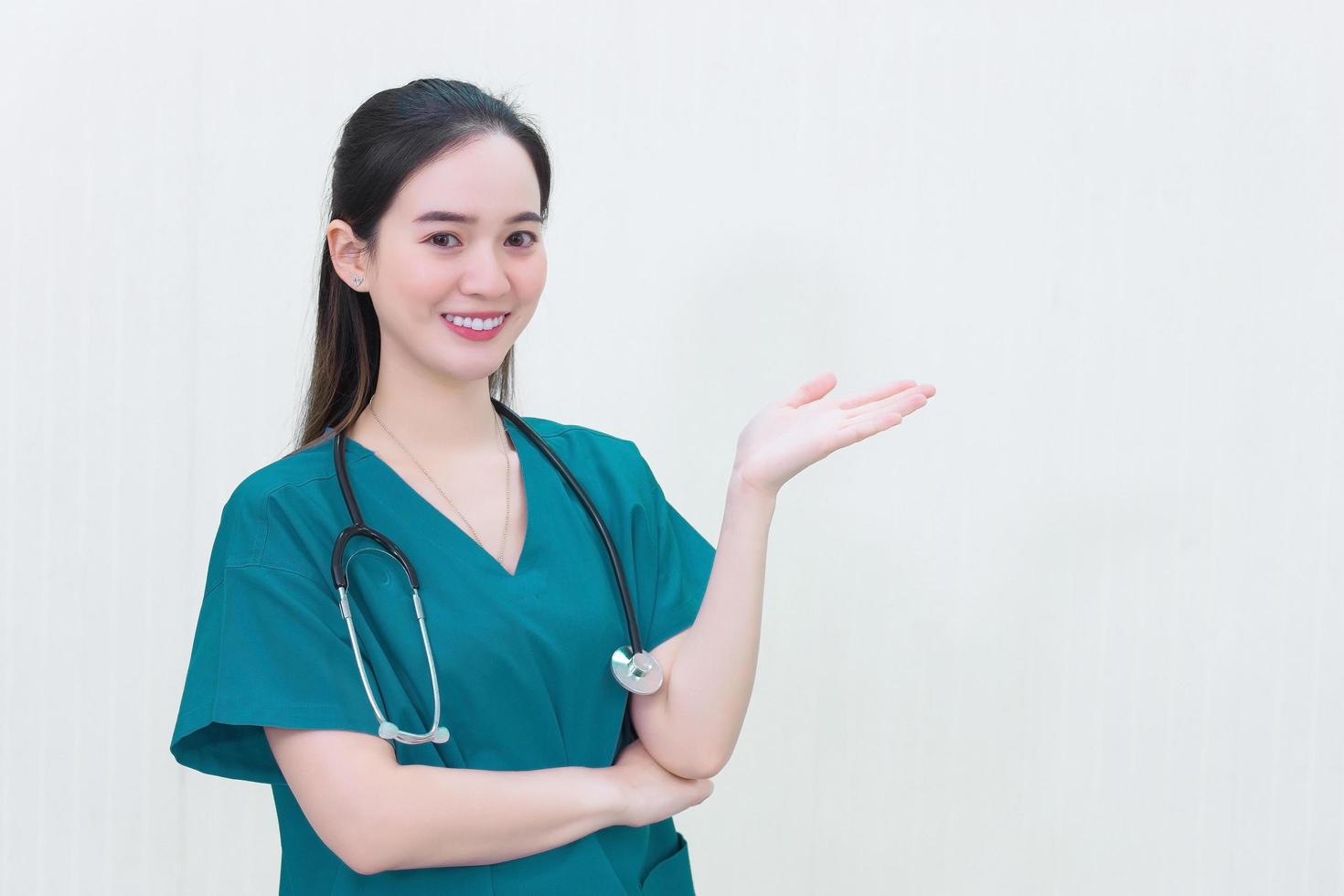 hermosa joven doctora asiática con uniforme azul se pone de pie y sonríe mientras señala la parte superior sobre un fondo blanco. foto