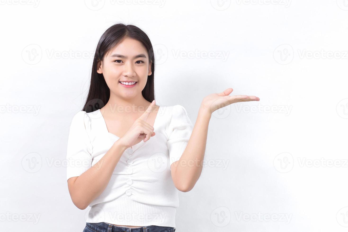 Asian woman in black long hair wears white shirt stands smiling and pointing up to present something on a white background. photo