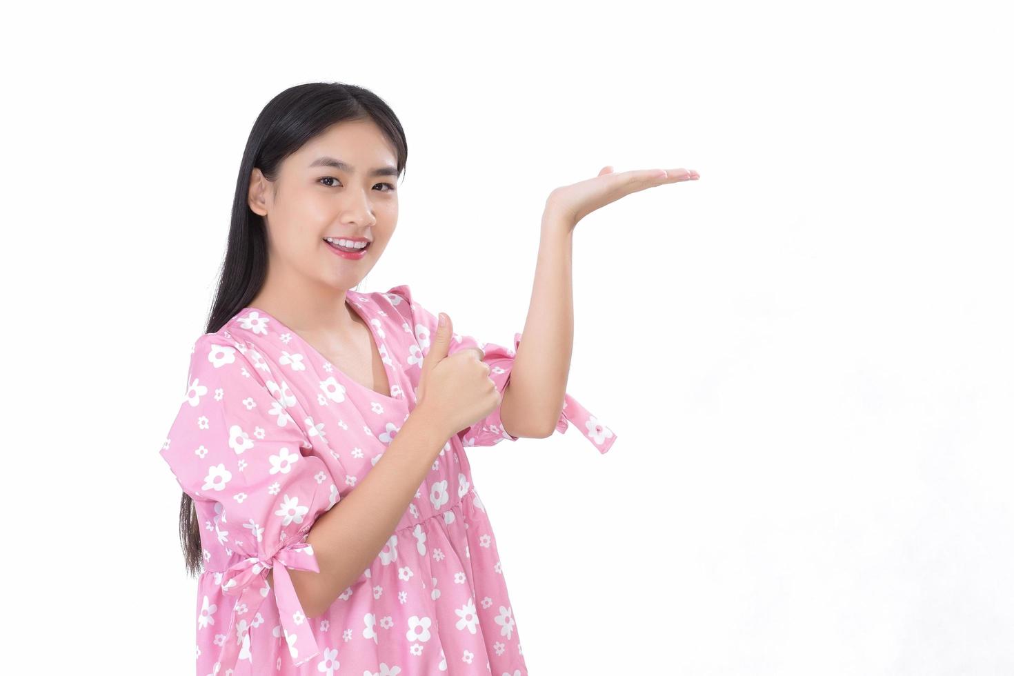 Asian beautiful woman with black long hair in white shirt shows thumb up and present something on white background. photo