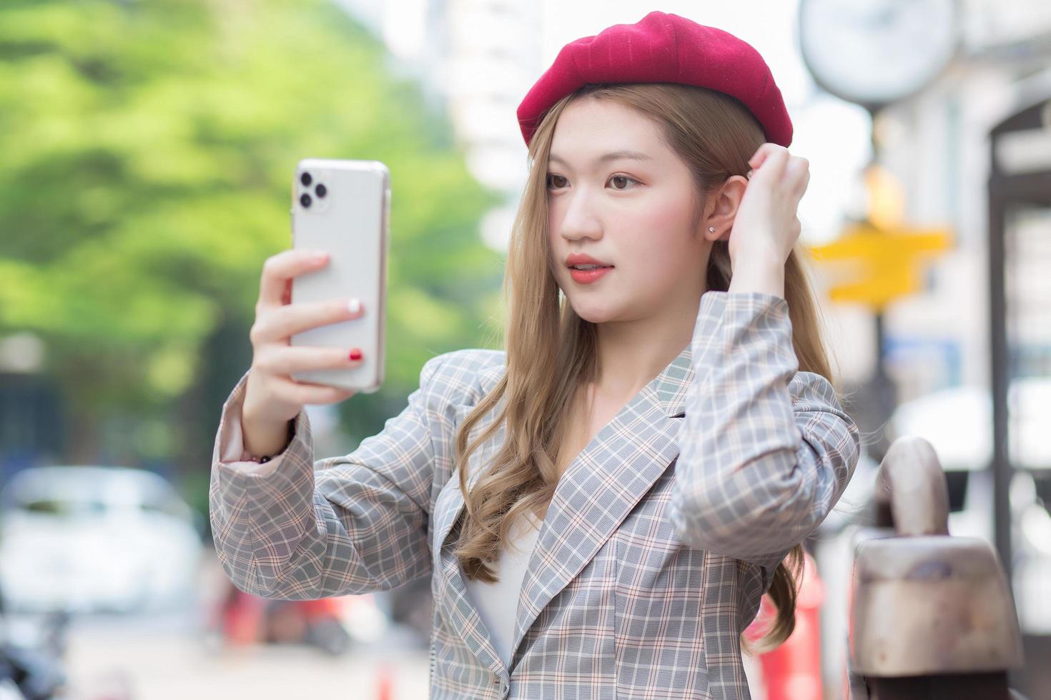 Asian woman in bronze hair takes selfie photo by smartphone on street as background.