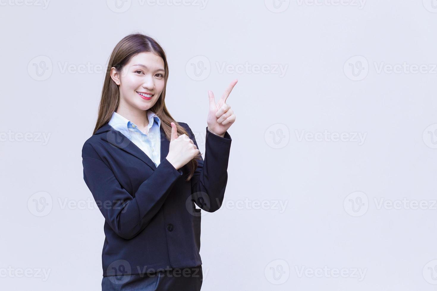 Asian working woman who has long hair wears black formal suit with blue shirt while she shows point up to present something on white background. photo