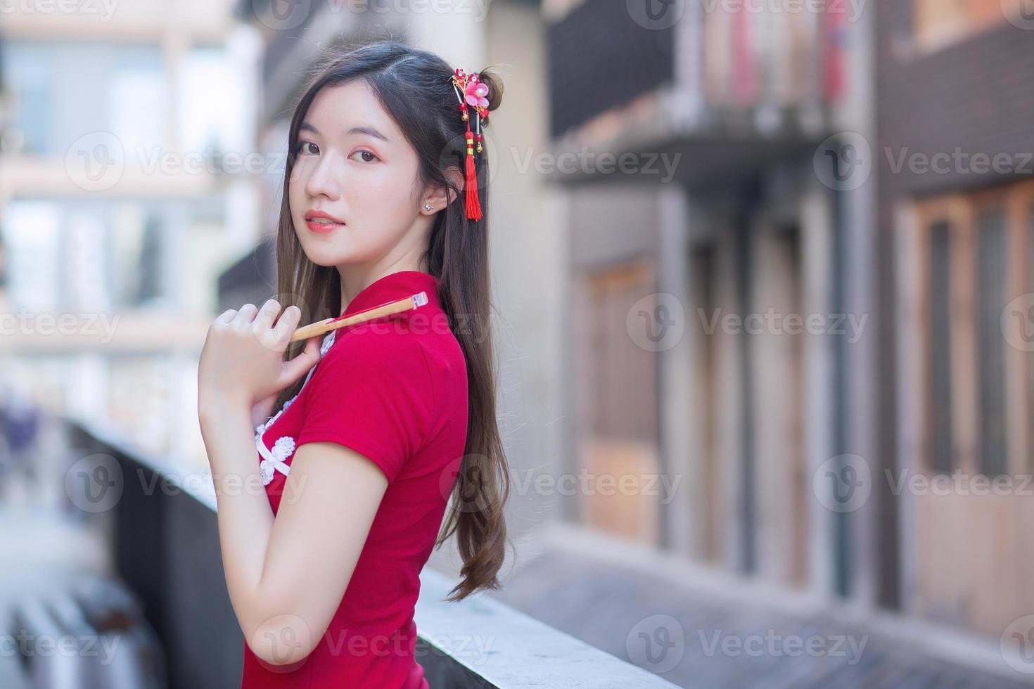 Beautiful Asian female in red dress stands holds a fan among old city center in Chinese new year theme. photo