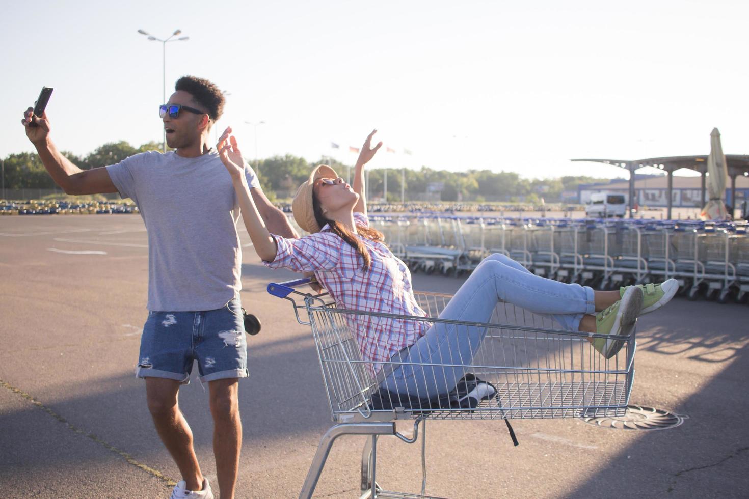 Happy young couple riding on trolley on empty mall parking , hipster friend have good time during shopping, couple in love riding on shopping cart photo