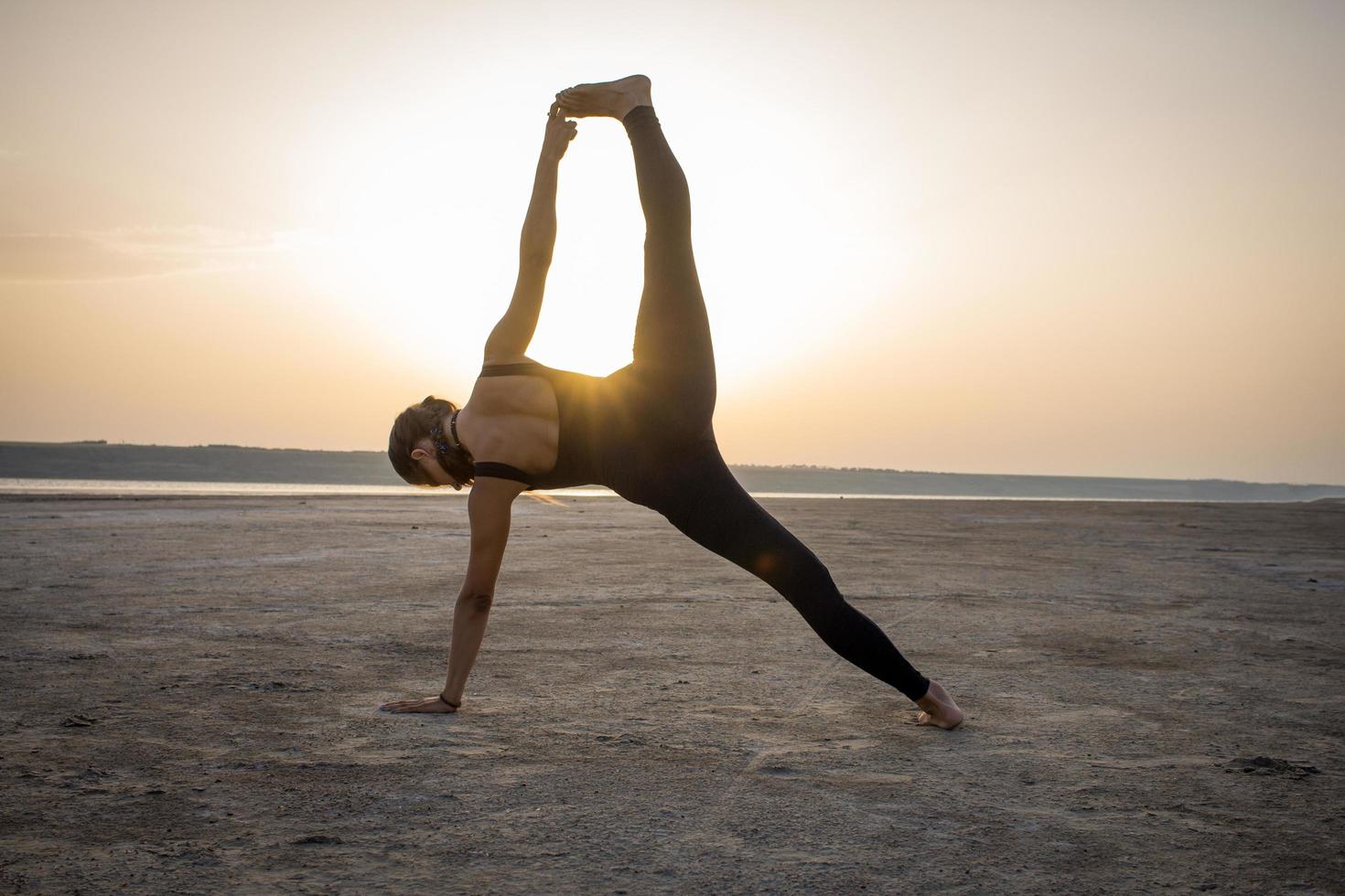 young fit woman training yoga poses in desert during the sunset or sunrise, female in black sportswear do stretching exercises photo