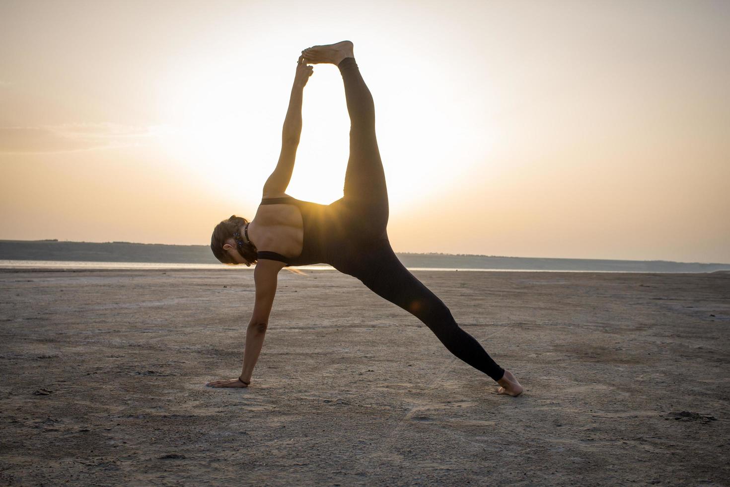 mujer joven en forma entrenando poses de yoga en el desierto durante la puesta de sol o el amanecer, mujer con ropa deportiva negra hace ejercicios de estiramiento foto