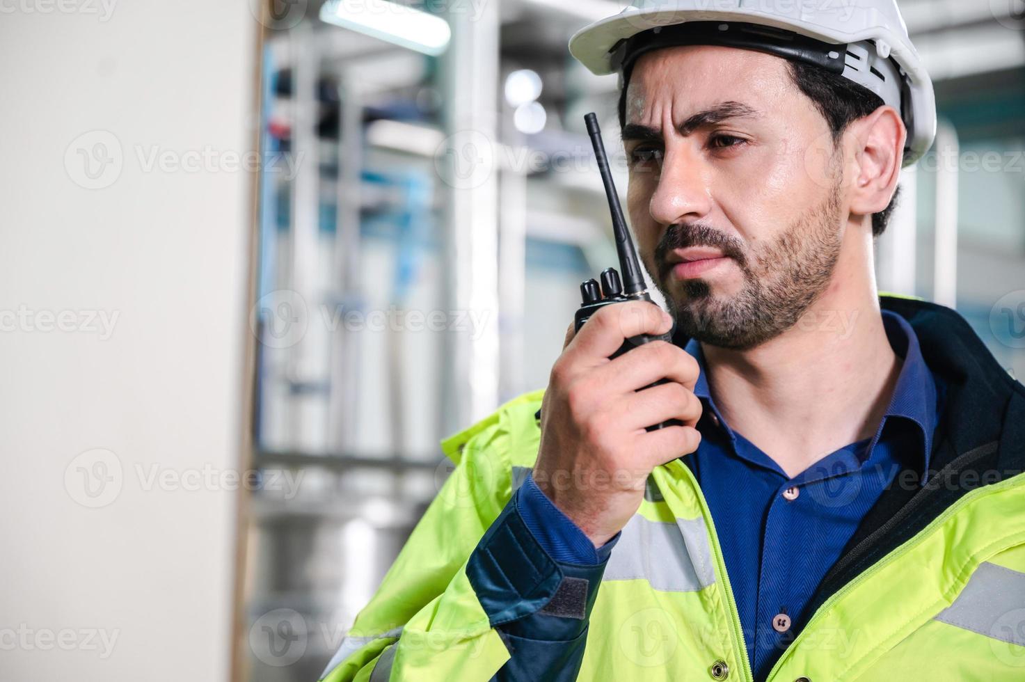 joven inspector de máquinas usando chaleco y casco con auriculares revisando la máquina y esterilizadores en la planta de agua mientras toma notas en una tableta digital foto