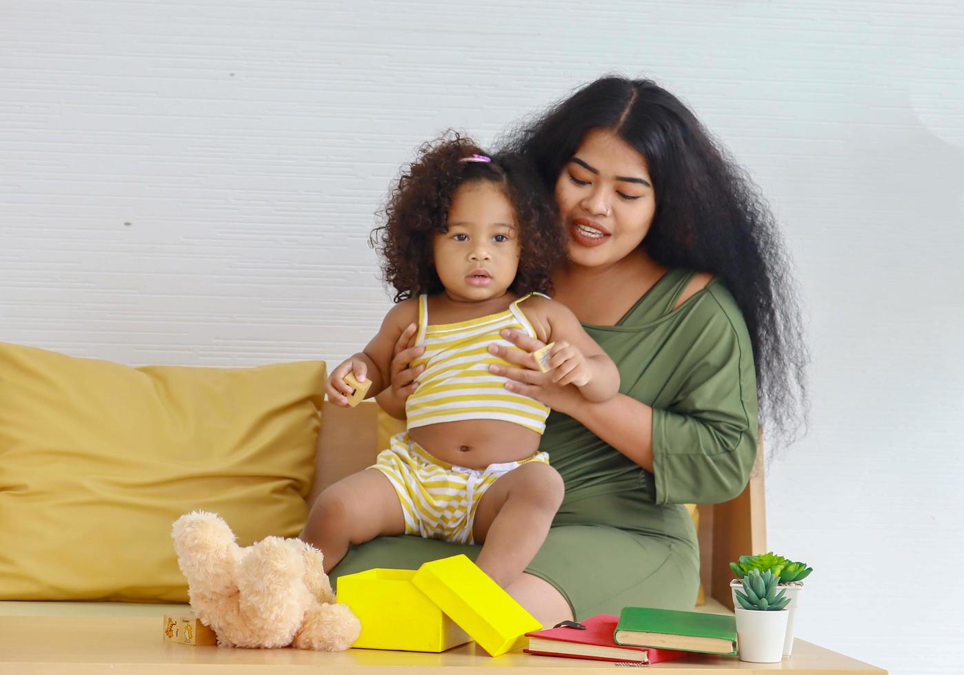 mother having fun playing with her daughter on holidays and yellow gift boxes Curly-haired daughter plays with her mother in the house. photo