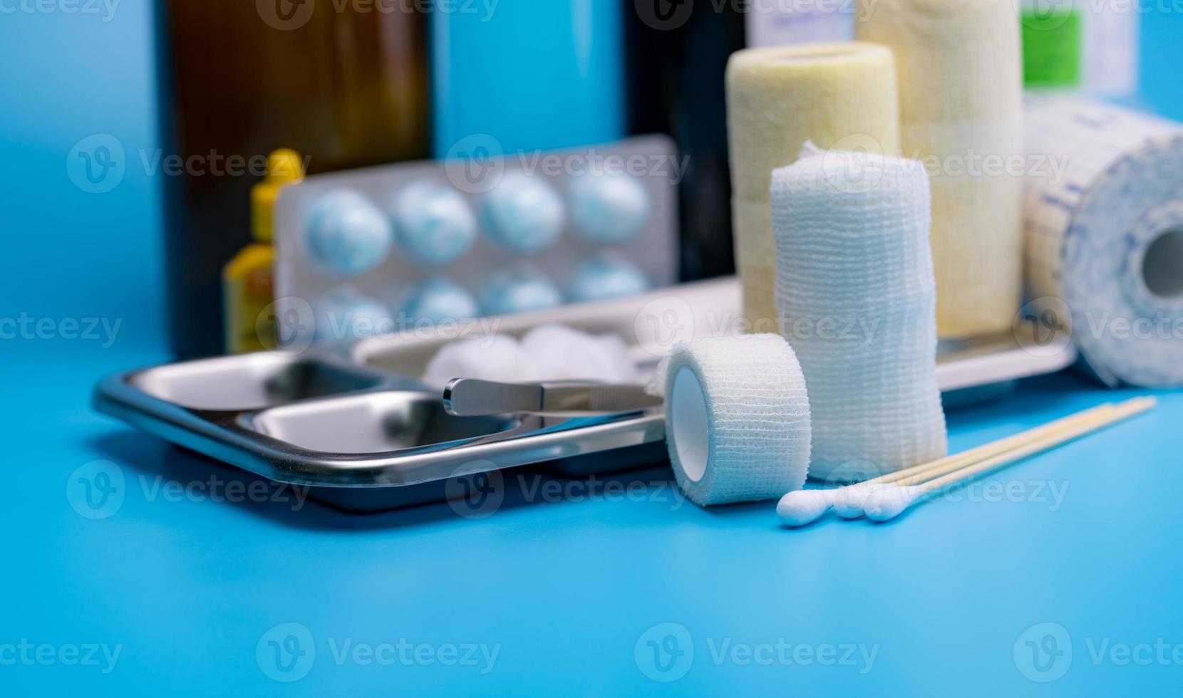 Wound care dressing set. Selective focus cotton stick and elastic conforming bandage, stainless steel plate on blur forceps, bandage, cotton ball with alcohol. Medical supply on blue background. photo