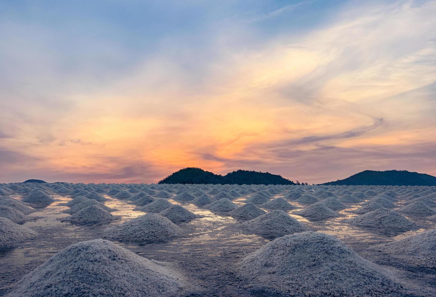 Salt farm in the morning with sunrise sky over the mountain. Organic sea salt. Evaporation and crystallization of sea water. Raw material of salt industrial. Solar evaporation system. Iodine salt. photo