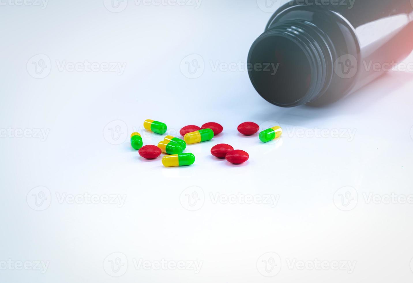 Red tablets and green-yellow capsule pills with amber plastic bottle on white table. Pharmaceutics concept. Pharmaceutical industry. Pharmacy products. Healthcare and medications. Drug interactions. photo