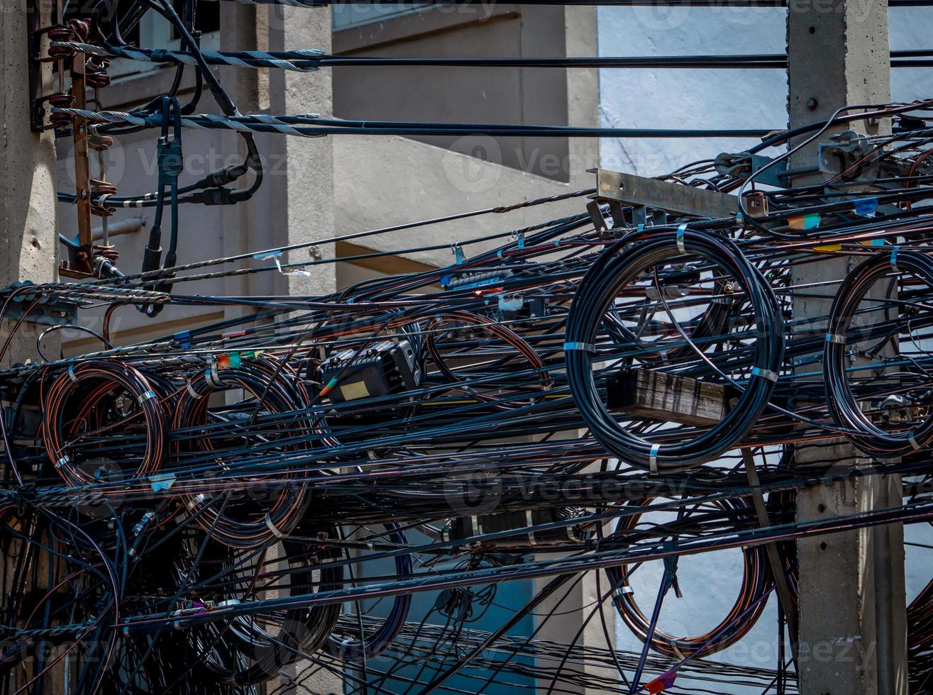 Tangled electrical wires on urban electric pole. Disorganized and messy to organization management concept. Tangled electrical wires in front of business office building. Should take underground wire. photo