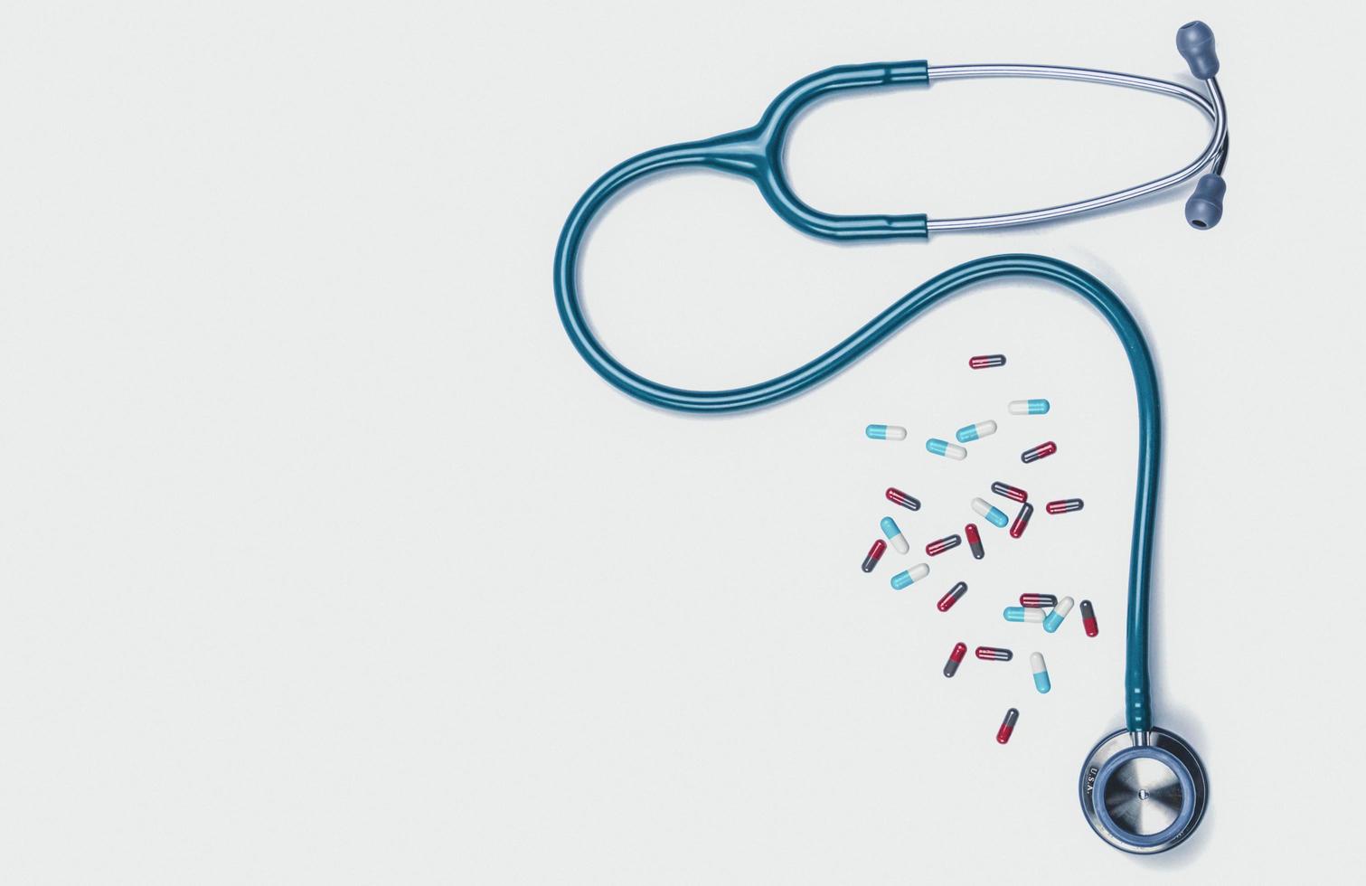 Green stethoscope with pile of capsule pills isolated on white background with copy space. Medical tool for doctor. Health check up concept. Medical equipment. Clinical Cardiology concept. photo