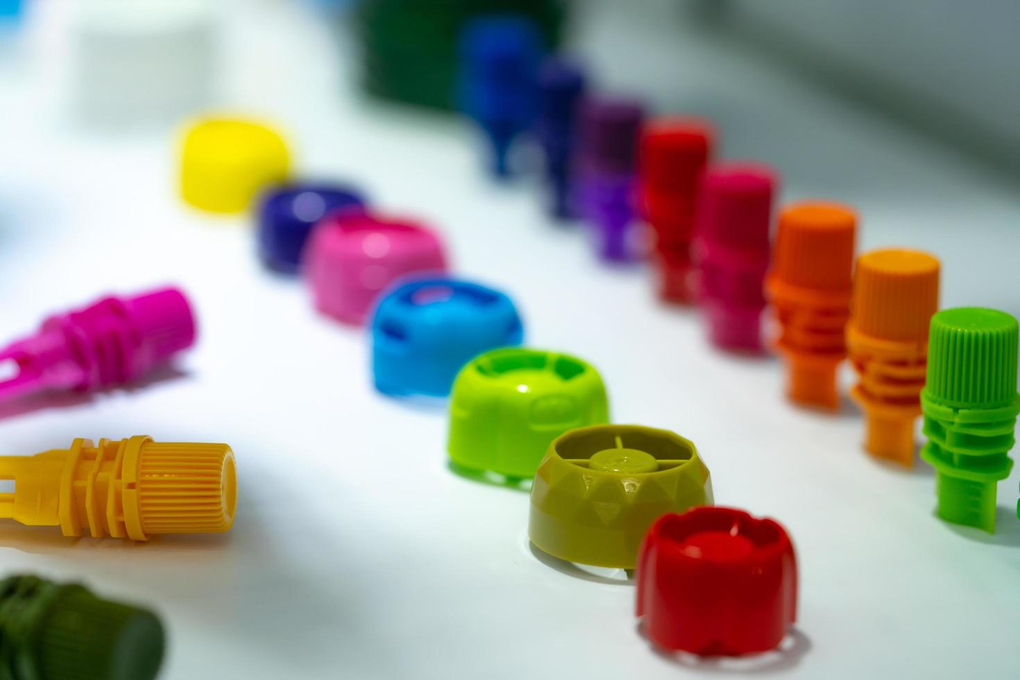 Selective focus on different type of plastic bottle cap of food and drink product. Green, yellow, red, pink, orange, blue, and purple cap closure on white table. Modern design plastic bottle cap. photo