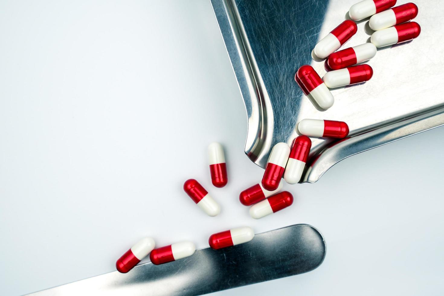 Red-white antibiotic capsule pills on stainless steel drug tray. Antibiotc drug resistance. Prescription drugs. Pharmaceutical industry. photo