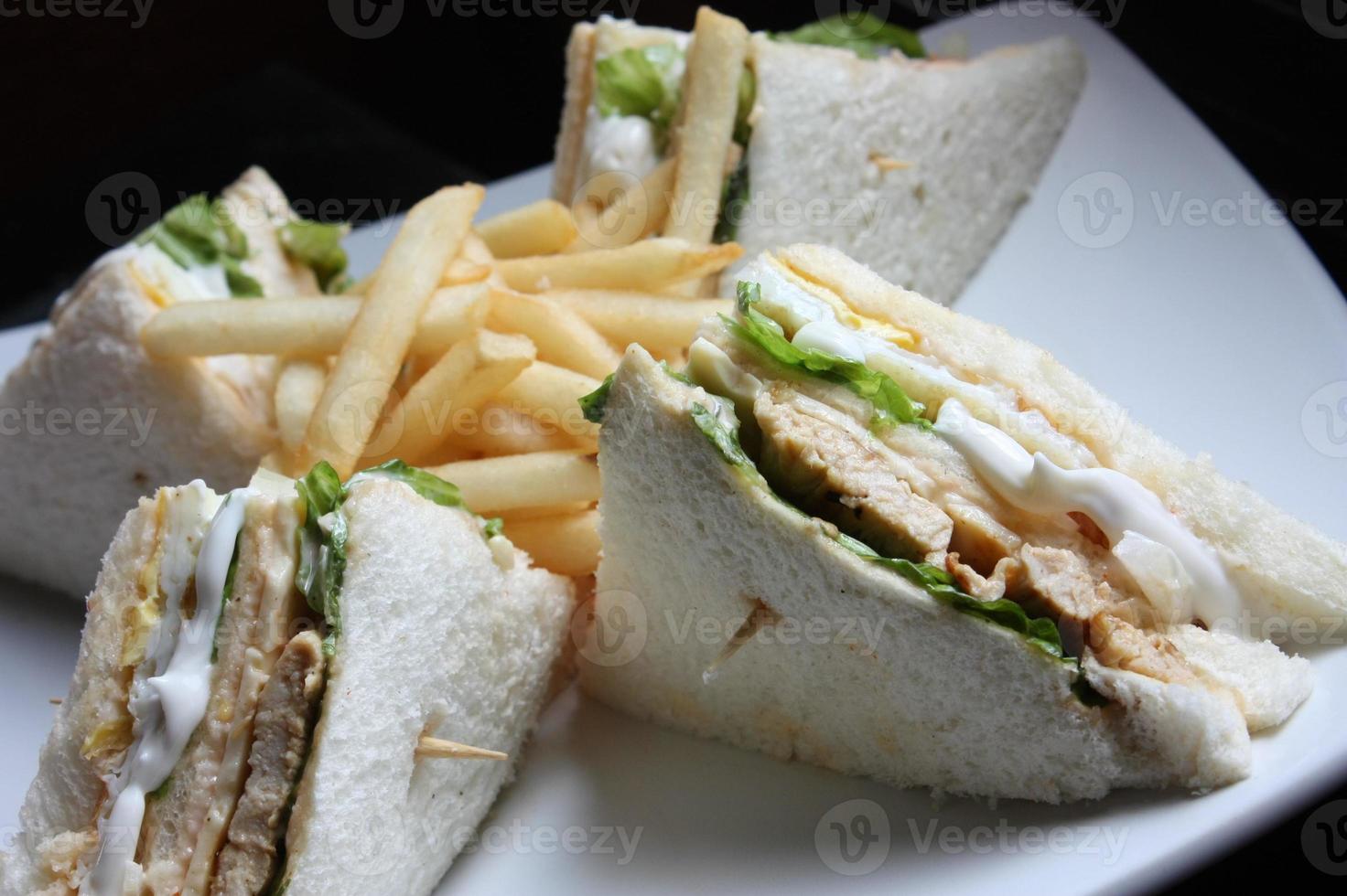 Triangular shaped sandwich. Stuffed thick meat, thin cheese, mayonnaise, lettuce. Pierced with a toothpick. On a white ceramic plate. close up. photo