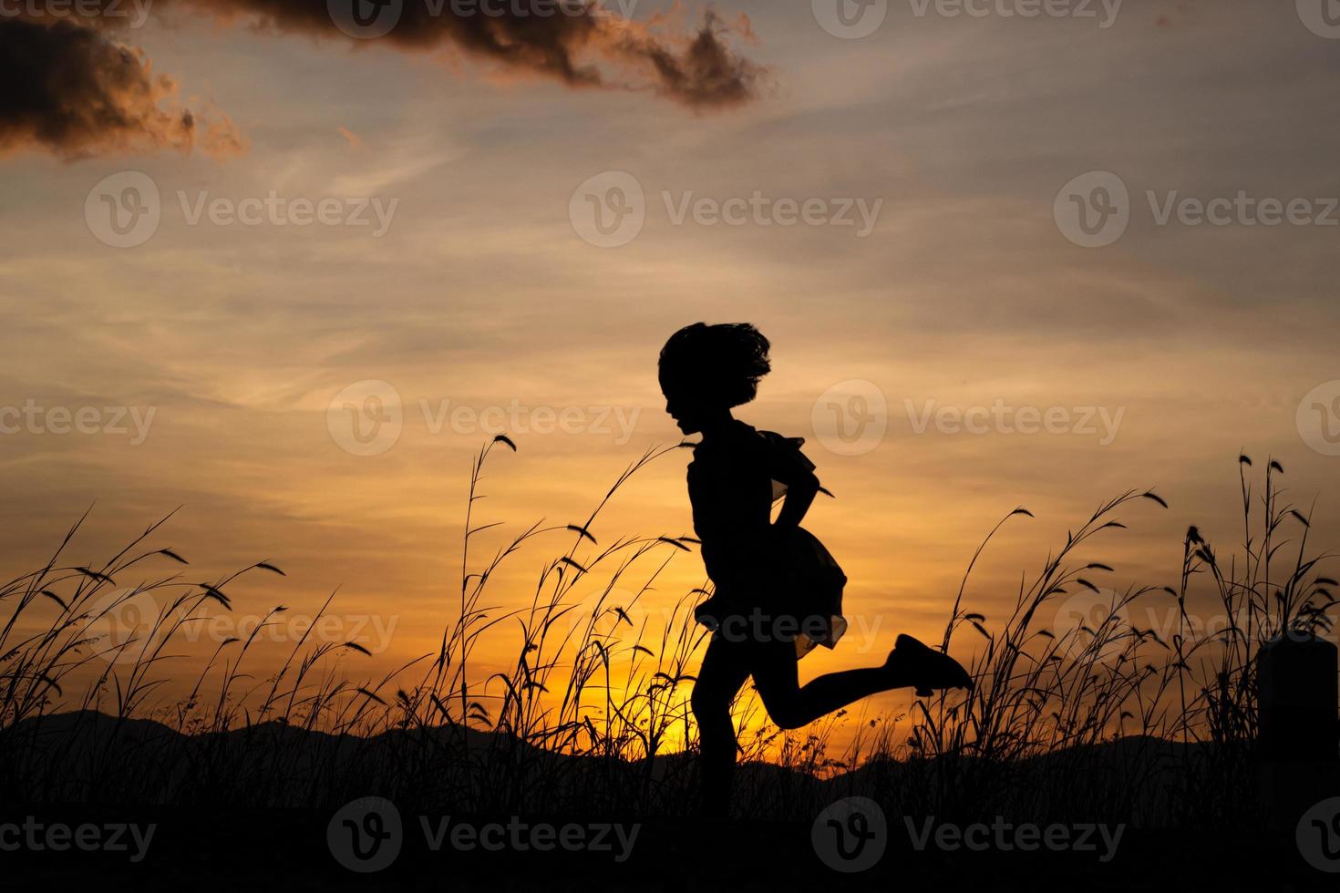 Silhouette of child girl running on the meadow at sunset background. photo