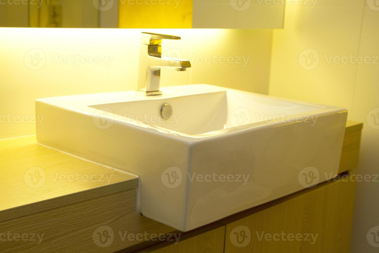 Close-up of a modern stainless steel faucet on white porcelain sink with warm light photo