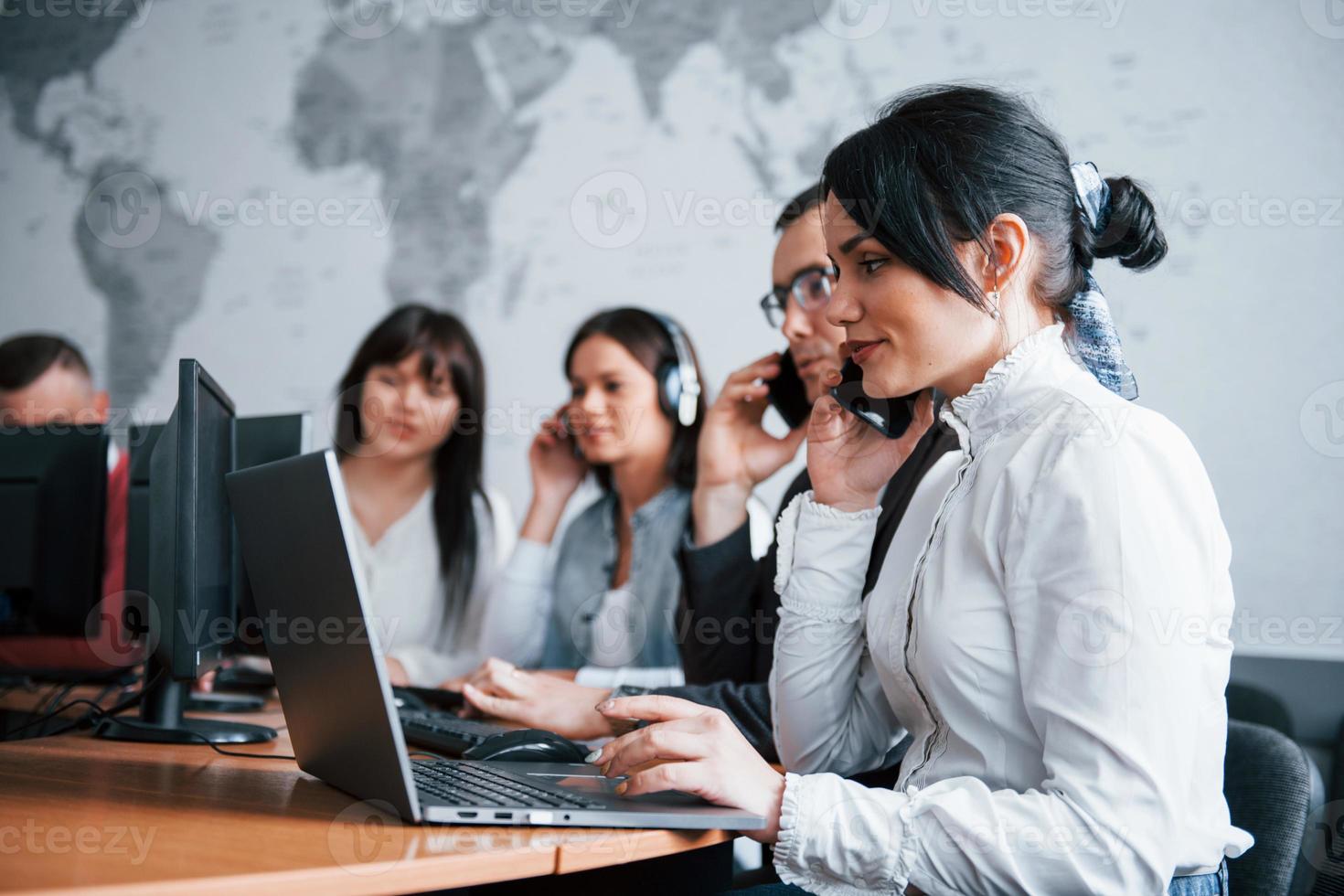 Beautiful brunette in focus. Young people working in the call center. New deals is coming photo