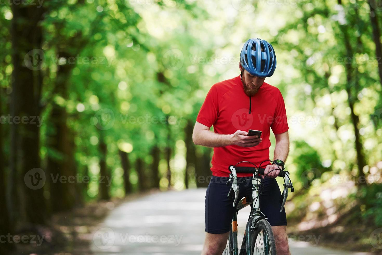Holding smartphone. Cyclist on a bike is on the asphalt road in the forest at sunny day photo