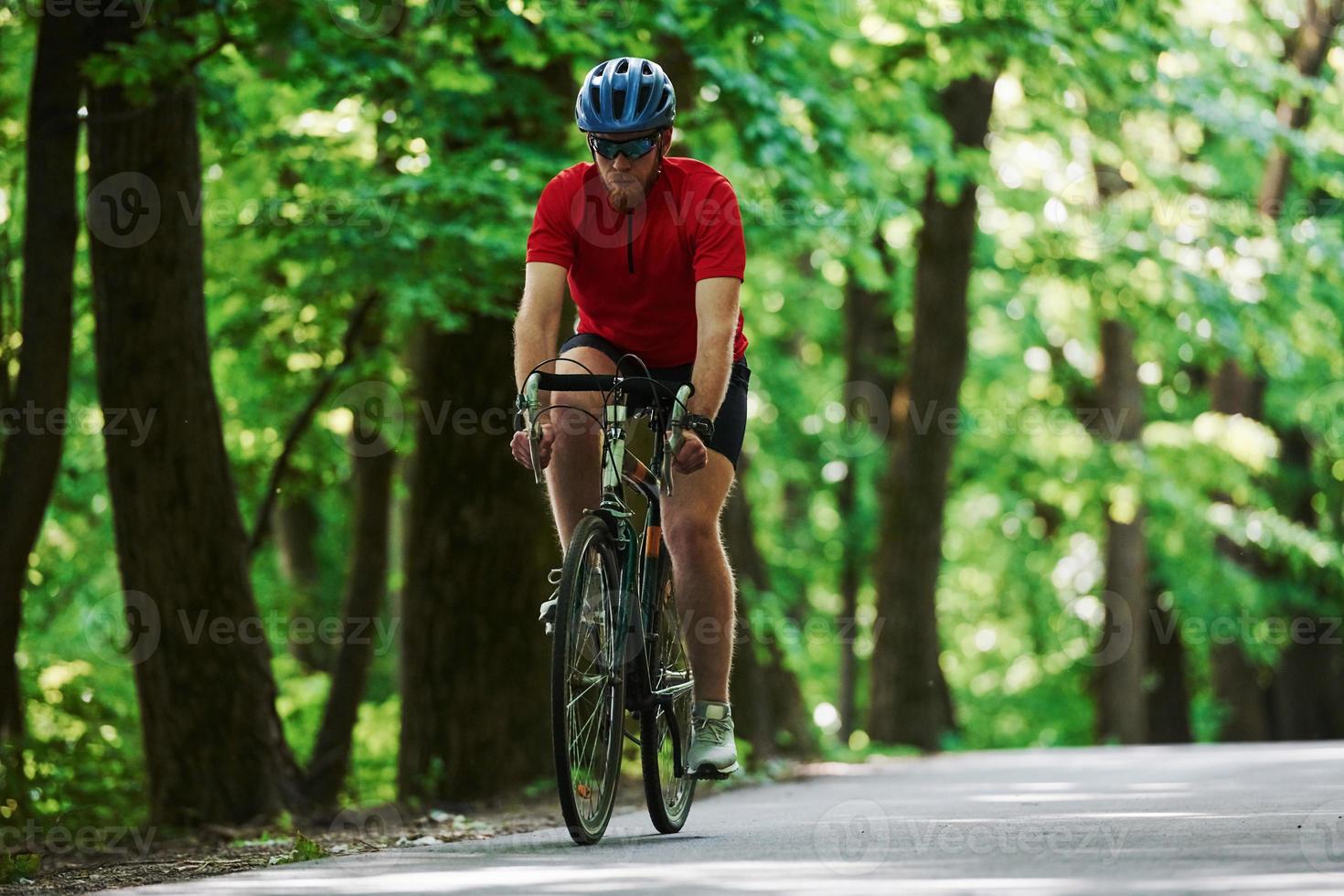 corriendo hacia adelante ciclista en bicicleta está en la carretera asfaltada en el bosque en un día soleado foto