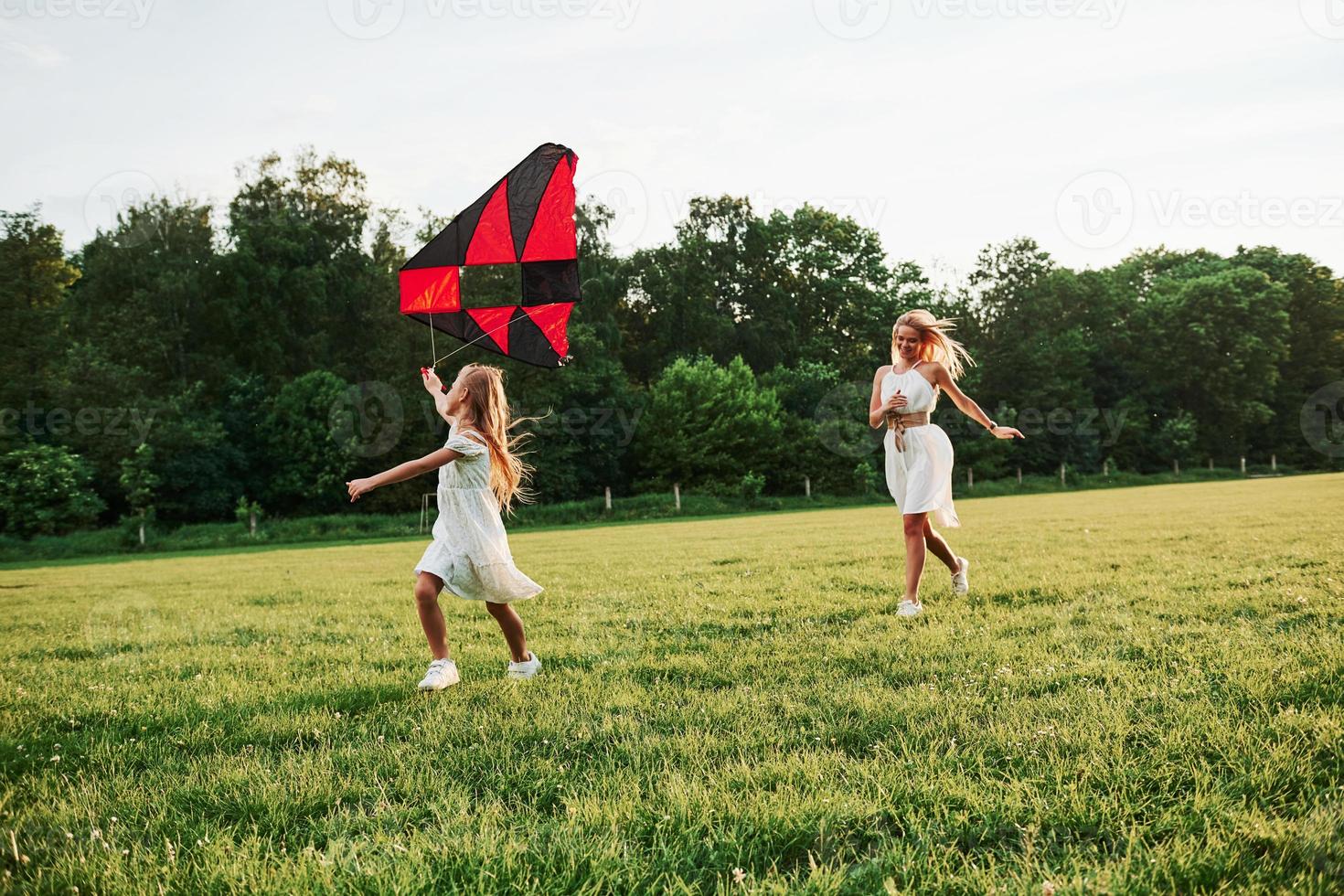 Running together. Mother and daughter have fun with kite in the field. Beautiful nature photo