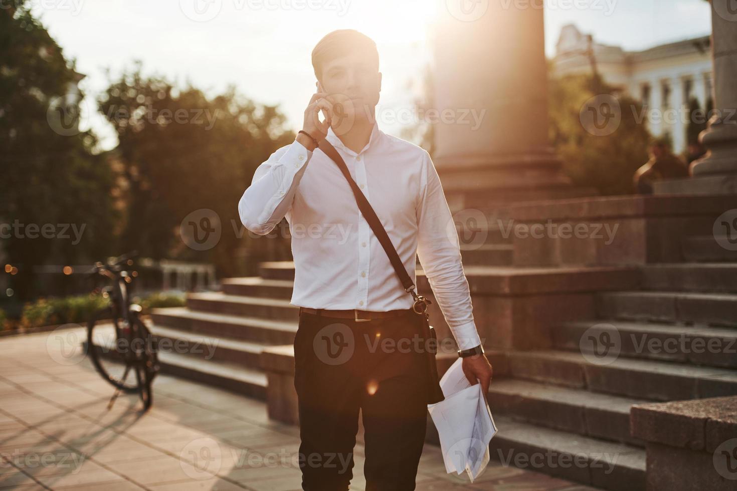 Nice sunbeam goes over head. Businessman in formal clothes with black bicycle is in the city photo
