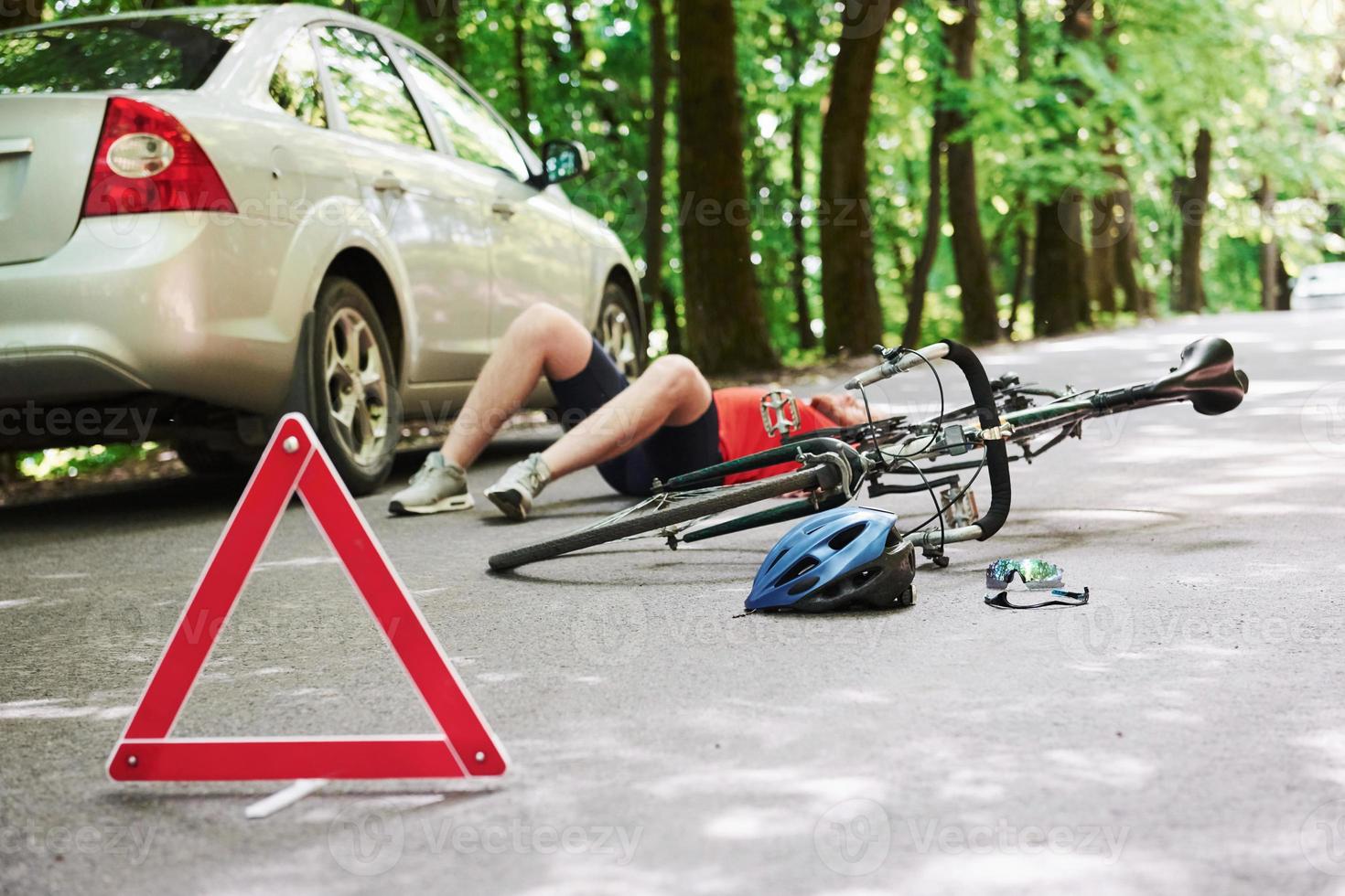 Man lying down. Victim on the asphalt. Bicycle and silver colored car accident on the road at forest at daytime photo