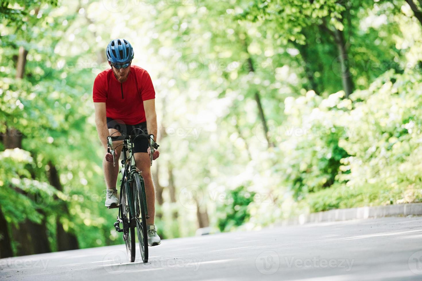 Stamina test. Cyclist on a bike is on the asphalt road in the forest at sunny day photo