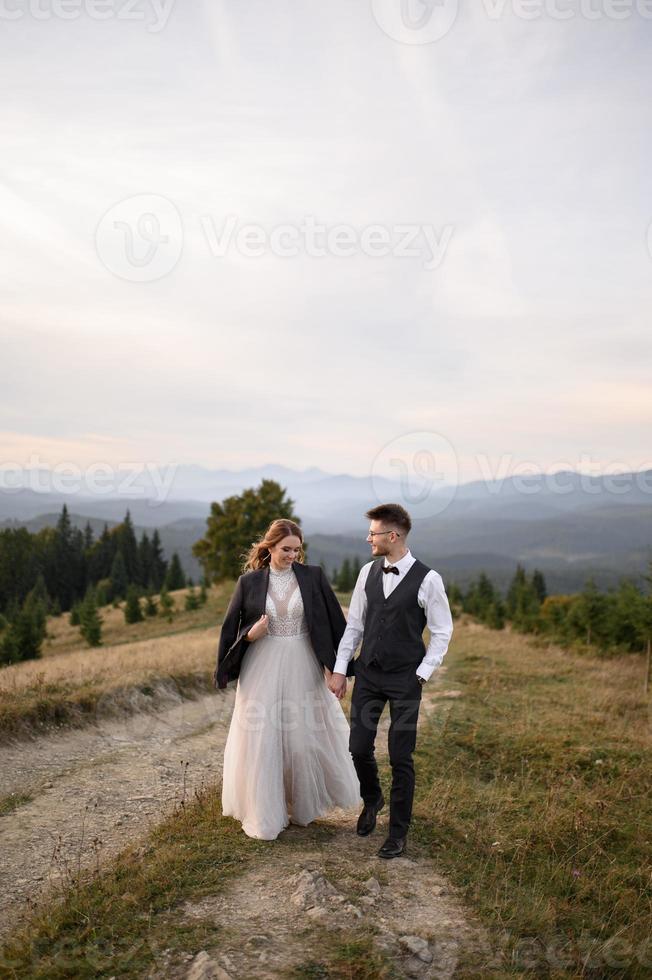 happy stylish bride and groom running and having fun in mountains on summer sunny day photo