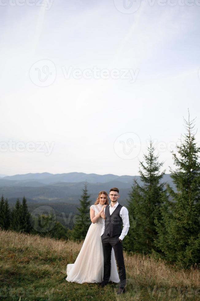 feliz novia y novio corriendo y divirtiéndose en las montañas en un día soleado de verano foto