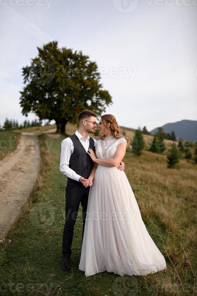 happy stylish bride and groom running and having fun in mountains on summer sunny day photo
